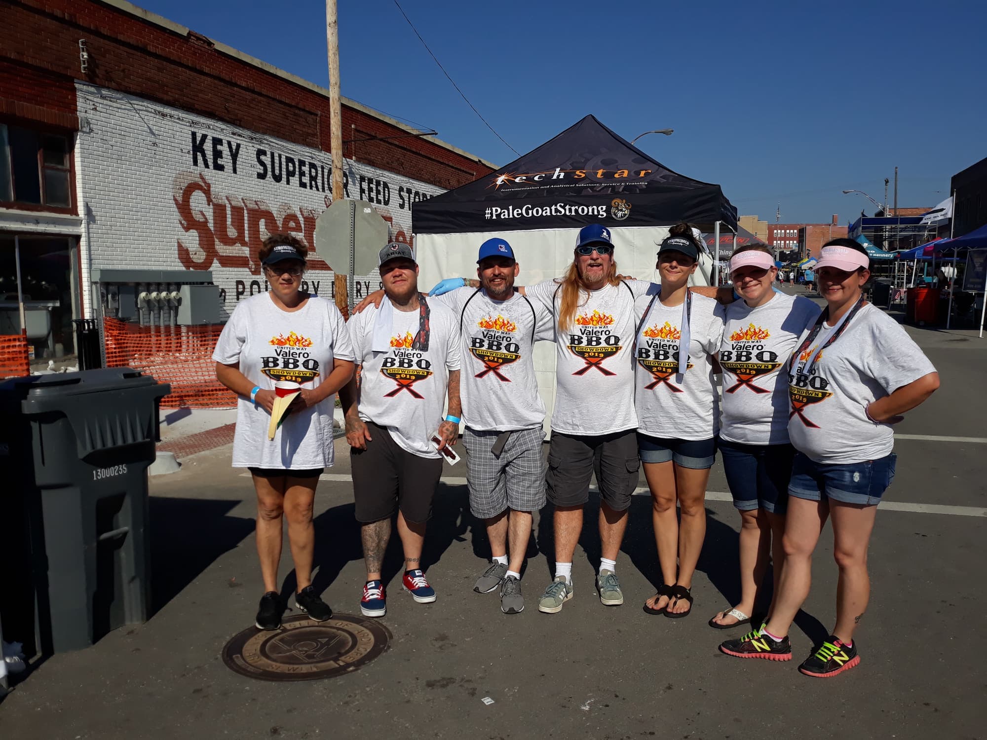 Seven volunteers in matching BBQ Showdown shirts lined up on the street