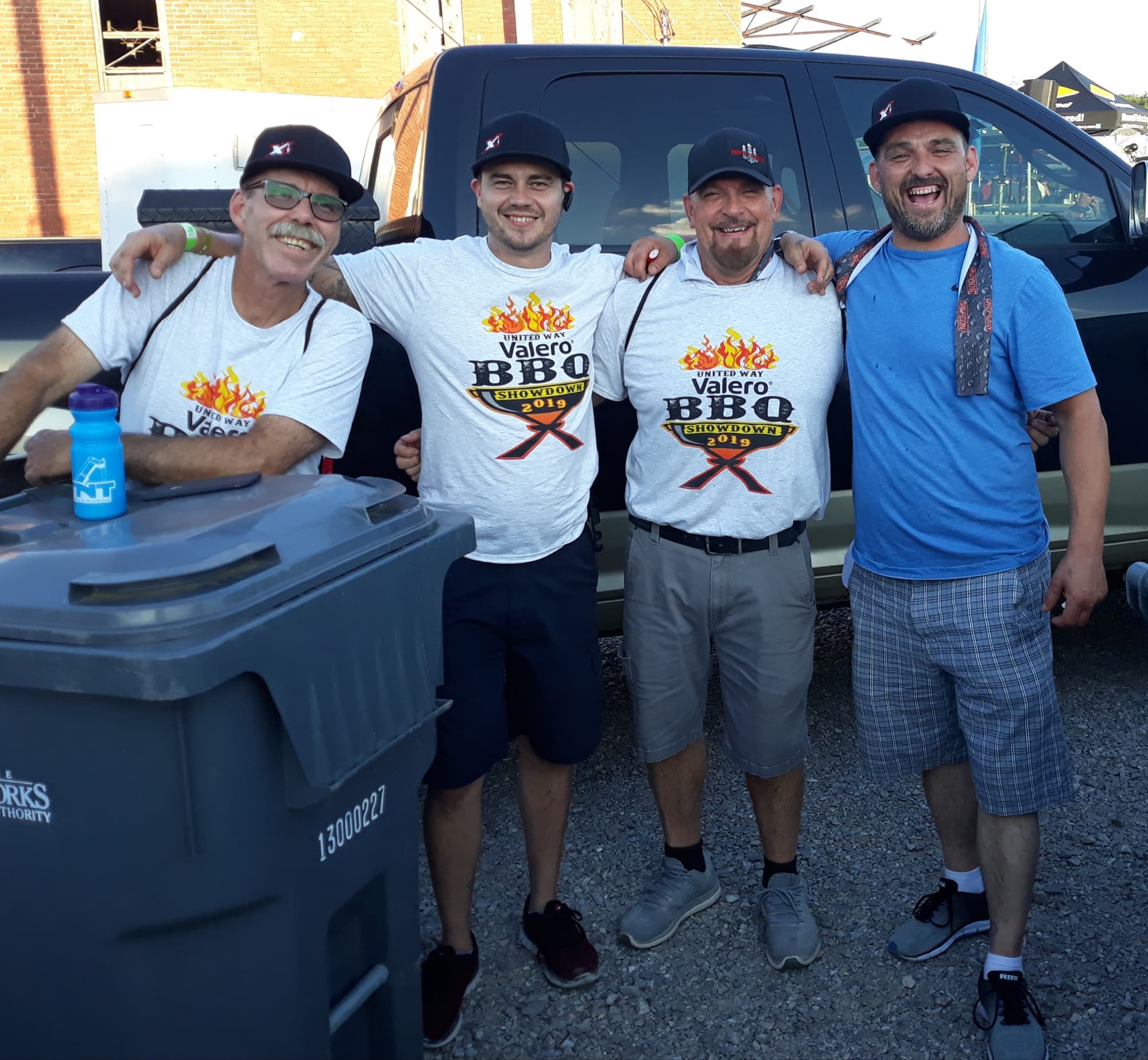Four volunteers with arms around each other in front of a truck at the BBQ Showdown
