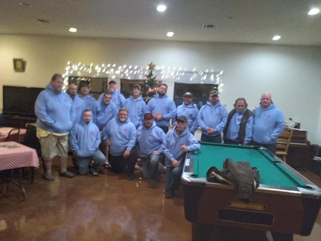 A large group of men in matching light-blue hoodies gathered around the pool table