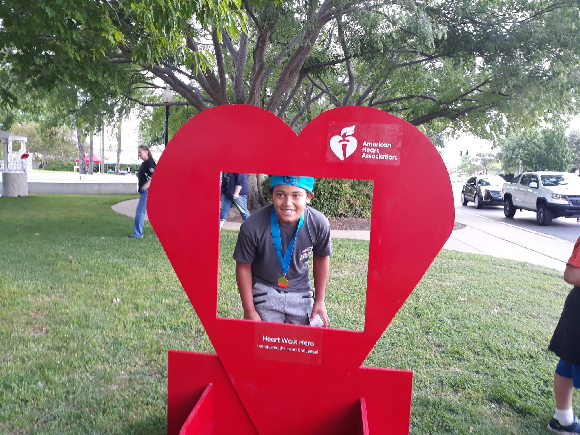 A smiling child looking through the giant red Heart Walk heart frame, wearing a medal
