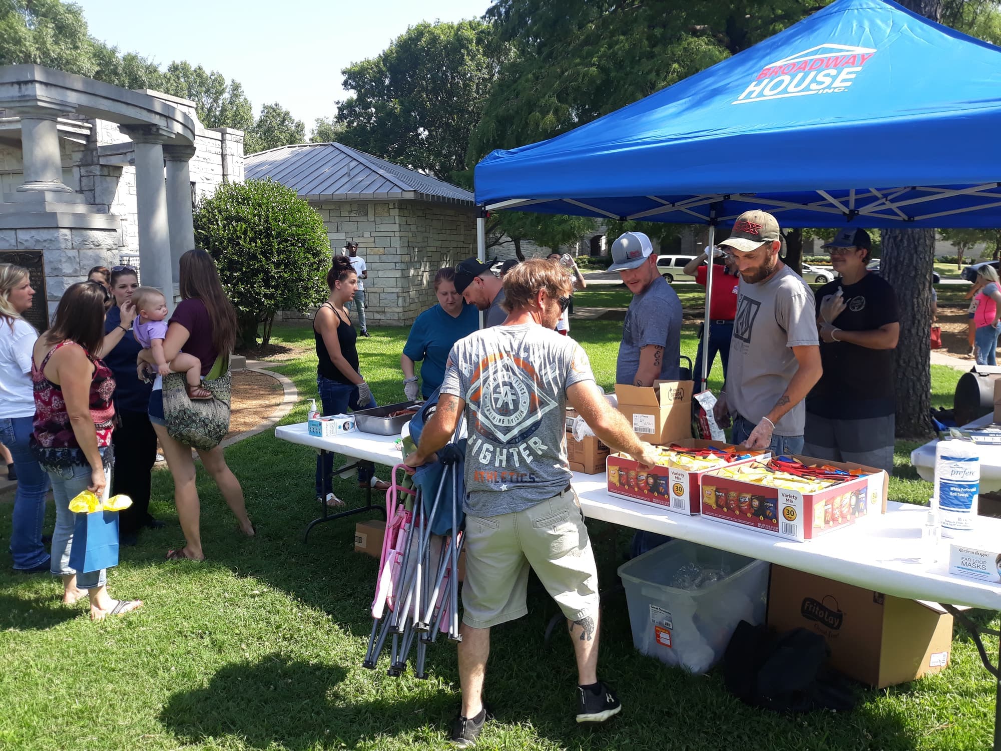 Neighbors gathered at a long table under the blue Broadway House tent